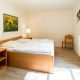 Schlafzimmer mit Holzbett und Nachttischen, weißer bettwäsche und grünem Vorhang