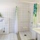 Barrierefreies Badezimmer mit Duschsitz, Waschbecken und WC mit Haltegriffen, alles weis gefliest