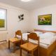 Schlafzimmer mit Doppelbett, 2 Stühlen und Schrank und 2 Nachttischen. weiße Bettwäsche und ein Blumenbild an der Wand.